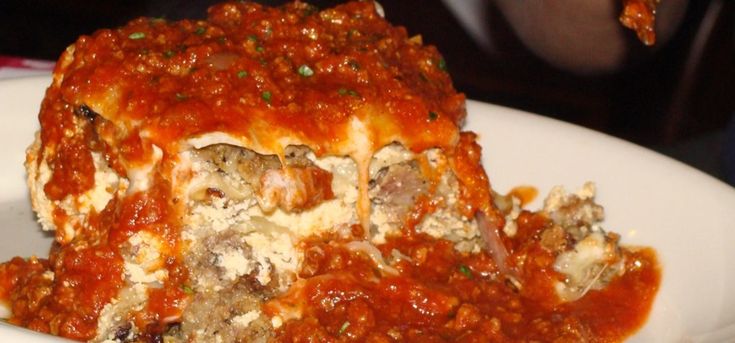 a white plate topped with lasagna covered in sauce and meatballs on top of it