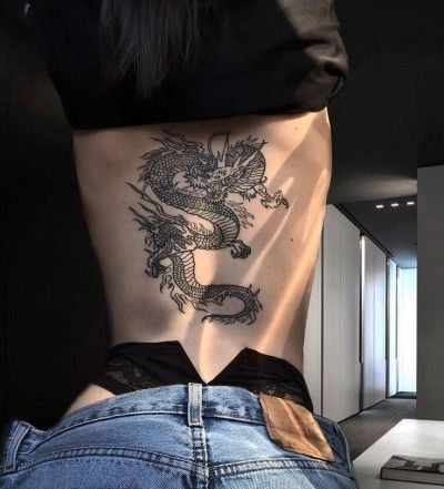 a woman with a dragon tattoo on her stomach and back, standing in front of a mirror