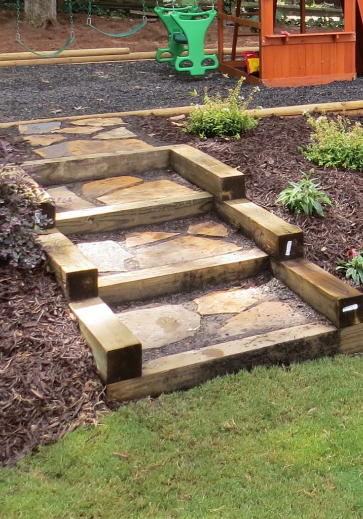 a garden with steps leading up to a play area and wooden structure in the background