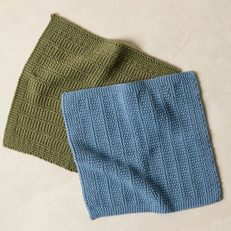 two green and blue knitted towels laying next to each other on a white surface