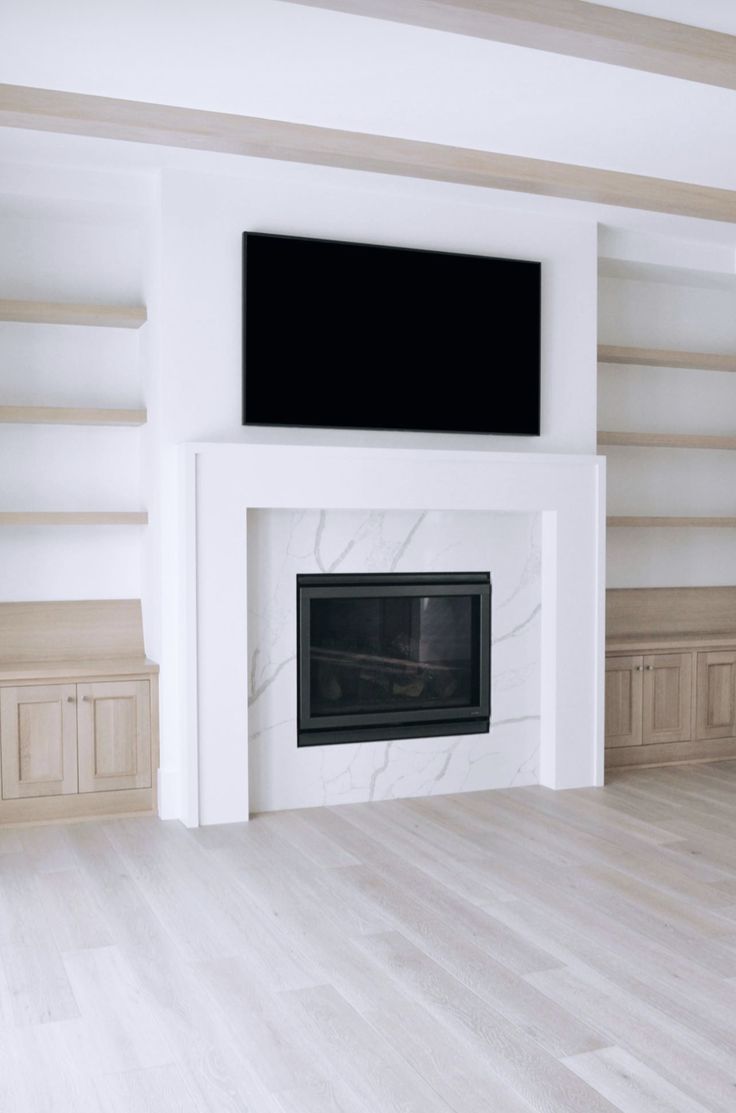 an empty living room with white walls and wood flooring, tv mounted above the fireplace