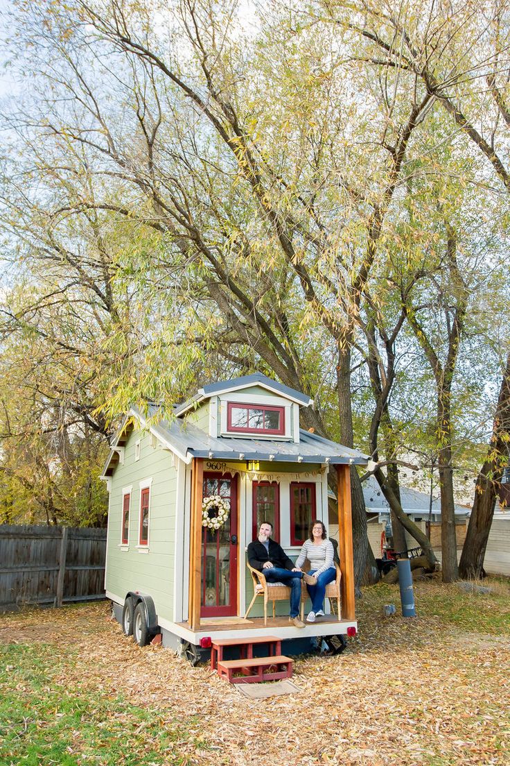 two people are sitting on the porch of a tiny house with trees in the background