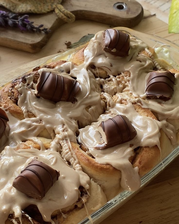 a glass dish filled with desserts covered in icing and chocolate candies on top of a wooden table