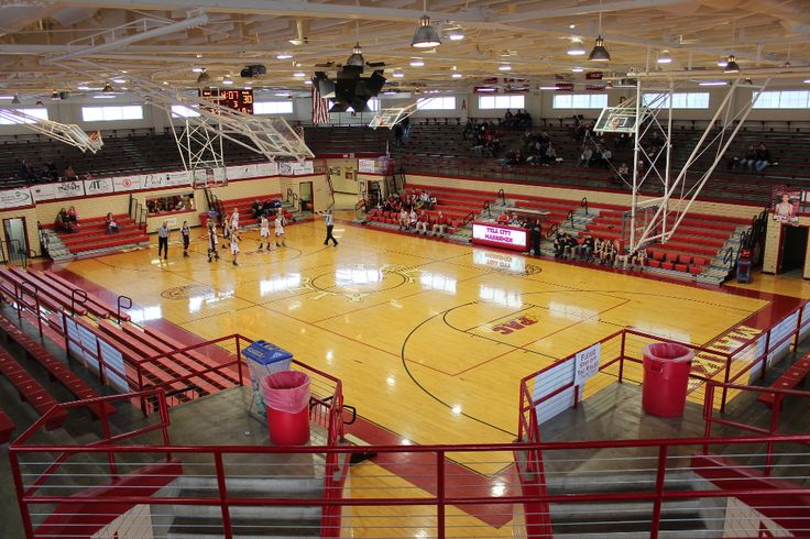 an indoor basketball court with red railings and people on the sidelines watching it