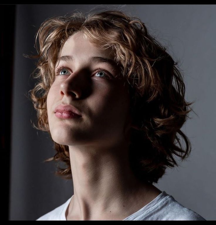 a young man with curly hair and blue eyes looking up to the side, wearing a white t - shirt