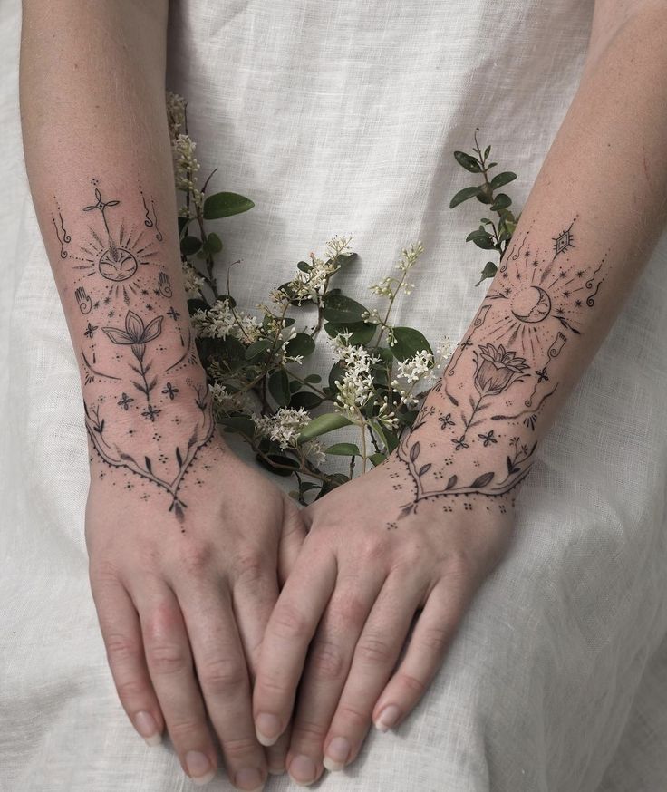 two hands with tattoos on them and flowers in the middle one is holding another hand