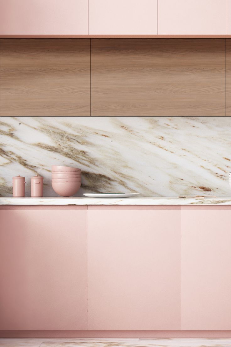 a kitchen with pink cabinets and marble counter tops, along with two cups on the sink