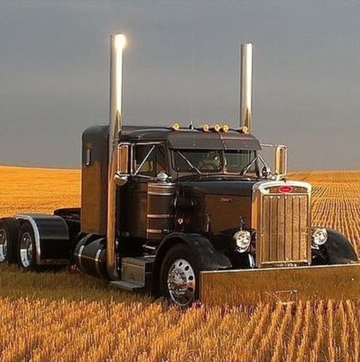 a tractor trailer parked in the middle of a wheat field with two lights on it's head