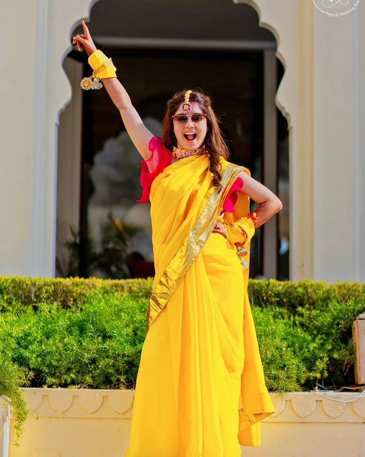 a woman in a yellow sari is holding her hand up to the side and smiling