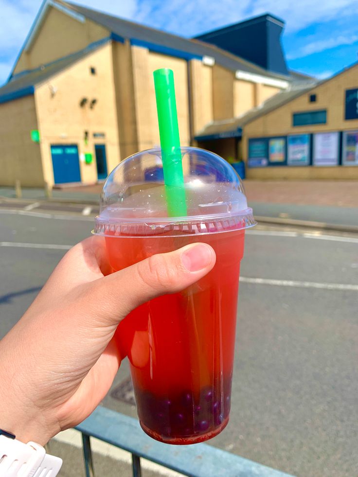 a person holding up a drink in front of a building with a green straw sticking out of it