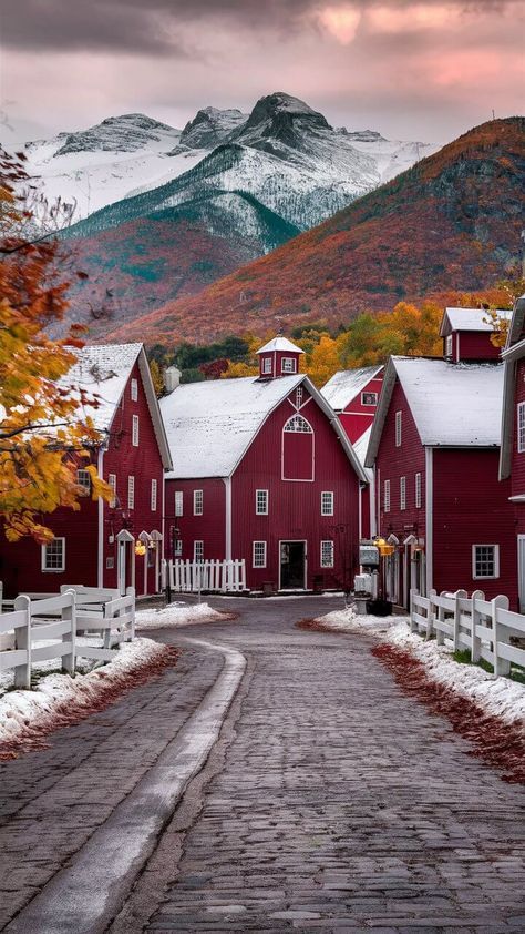 a red barn with snow on the ground and mountains in the background