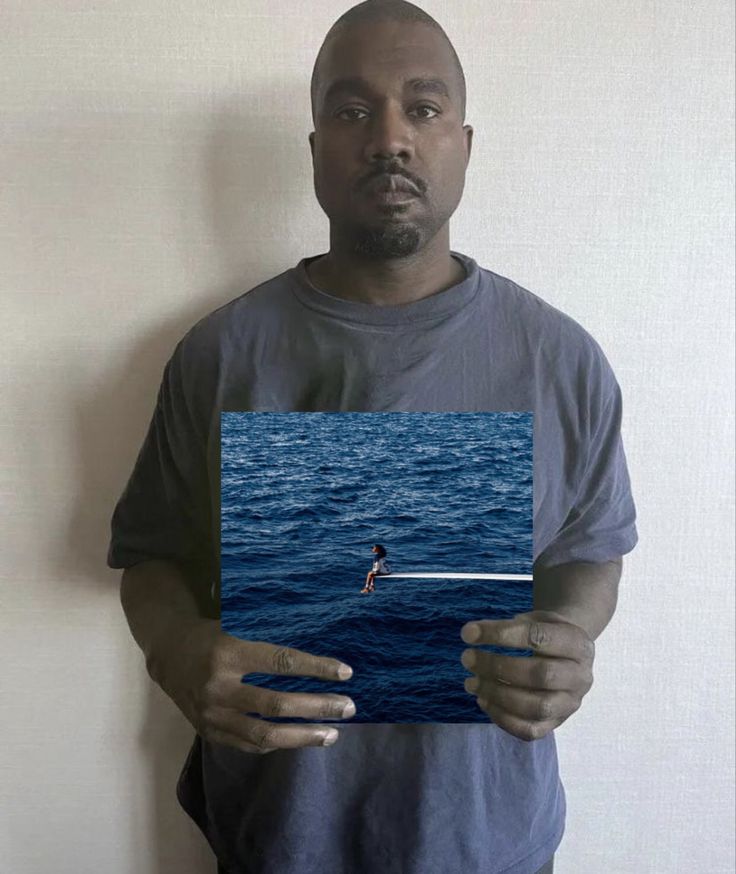 a man standing in front of a white wall holding up a piece of paper with an image of a person on it