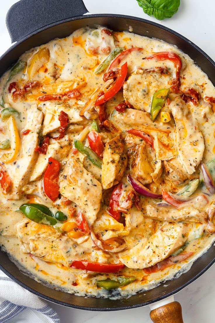 a skillet filled with chicken and vegetables on top of a table next to bread