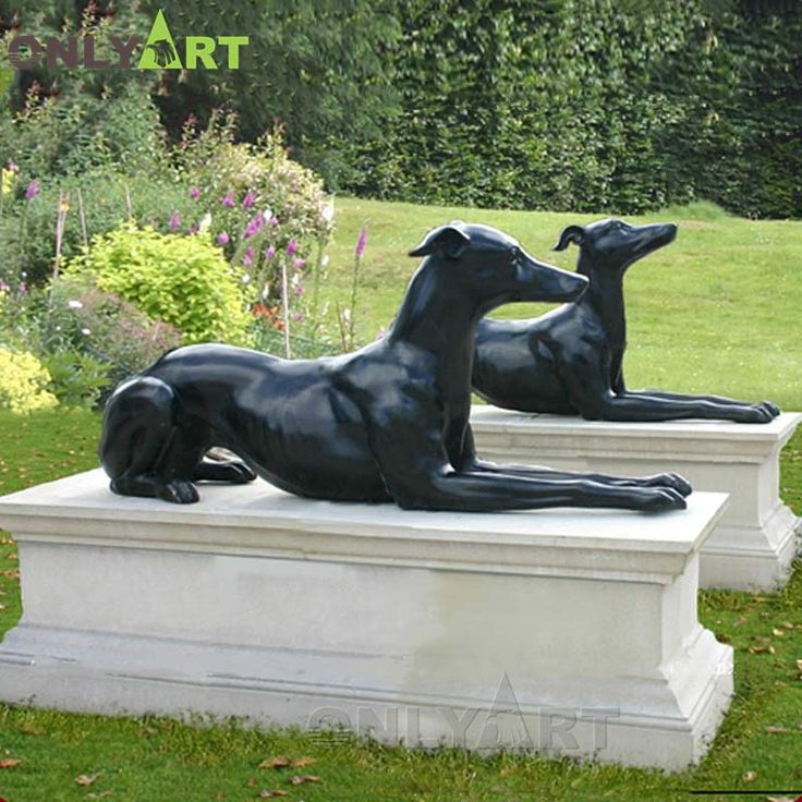 two statues of dogs laying on top of each other in the grass next to flowers