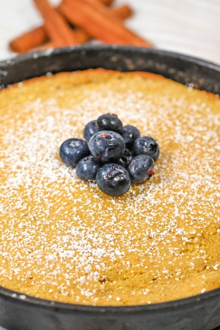 a blueberry pie with powdered sugar on top and carrots in the background