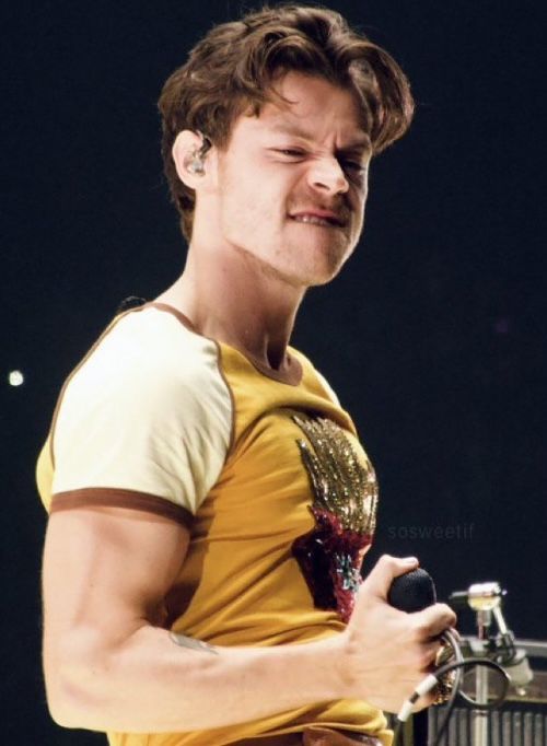 a young man holding a microphone in his right hand and wearing a yellow shirt on stage