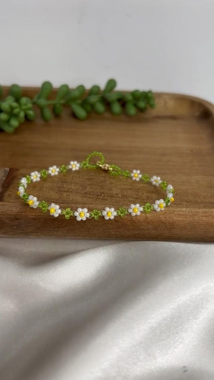 a wooden tray with some flowers and green leaves on it's side, sitting on a white sheet