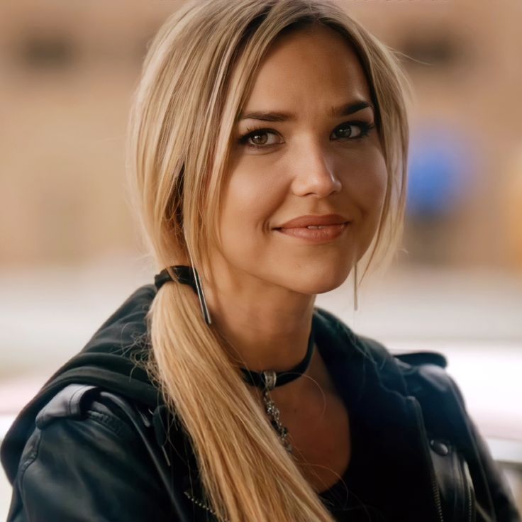 a woman with long blonde hair is standing in front of a car and looking at the camera