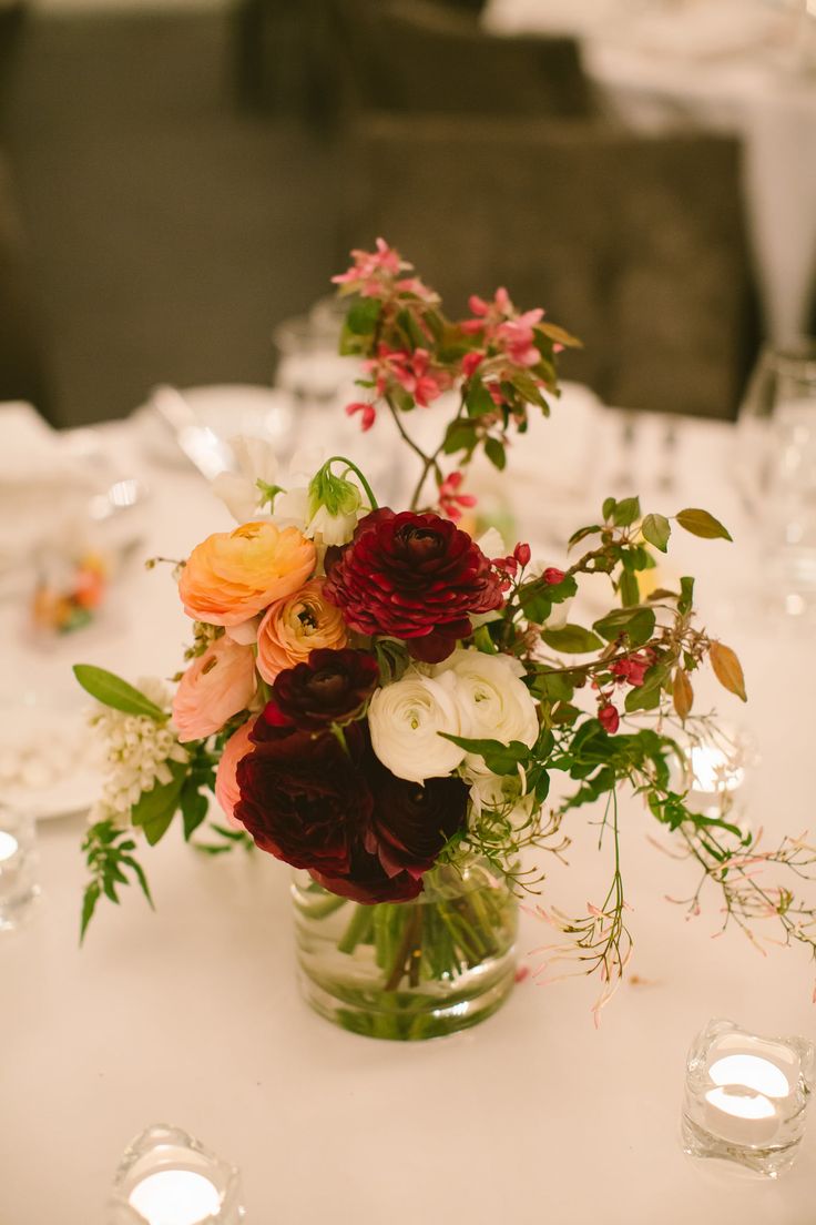 a vase filled with lots of flowers on top of a white tablecloth covered table