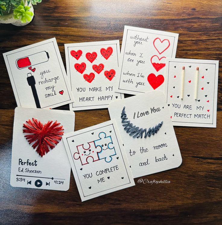 four cards with different designs on them sitting on top of a wooden table next to a potted plant