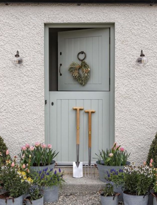 the front door of a white house with flowers and gardening tools