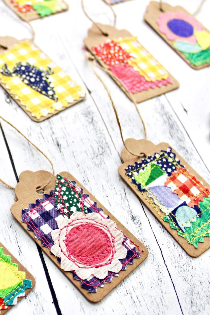 some tags are hanging on a white wooden table with colorful fabric and paper pieces attached to them