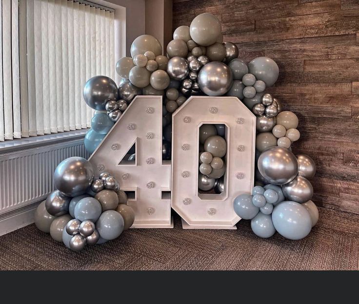 the number 40 is surrounded by balloons and silver balls in front of a wooden wall