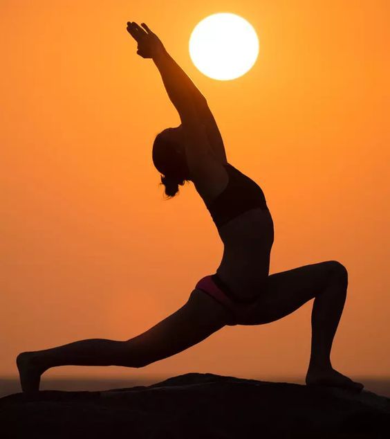 a woman doing yoga in front of the sun