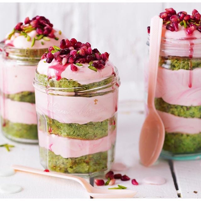 three mason jars filled with food and topped with pomegranates, sitting on a white table