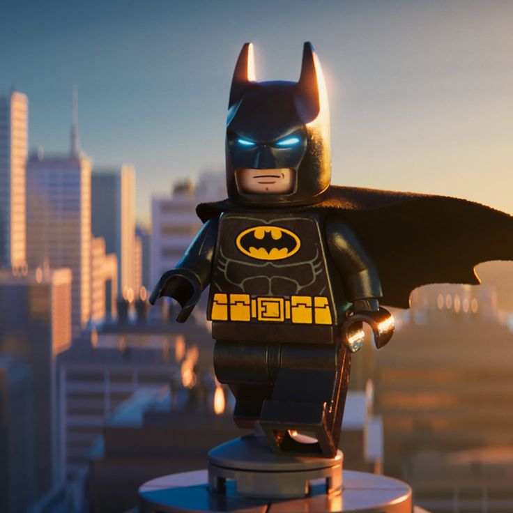 a lego batman standing on top of a metal object in front of a cityscape