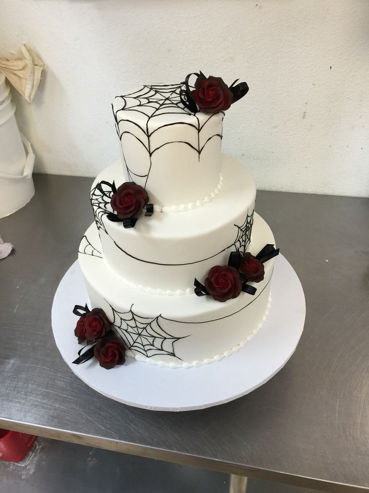 a three tiered cake decorated with red roses and spider webs on a table