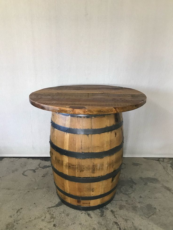 a wooden barrel table sitting on top of a cement floor next to a white wall