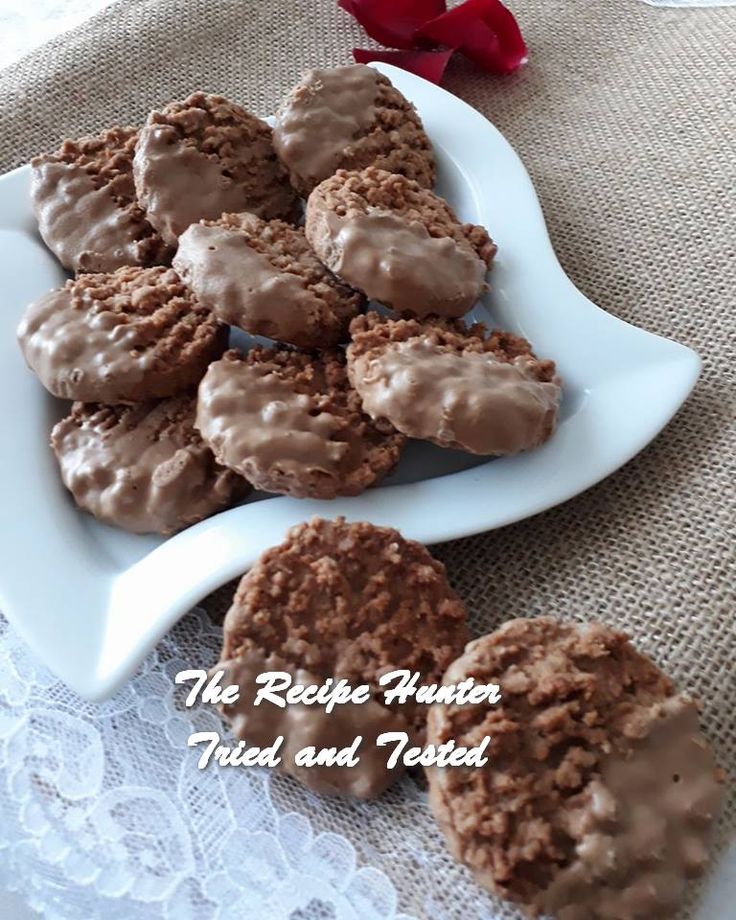 cookies with chocolate frosting on a white plate next to a red rose and lace tablecloth