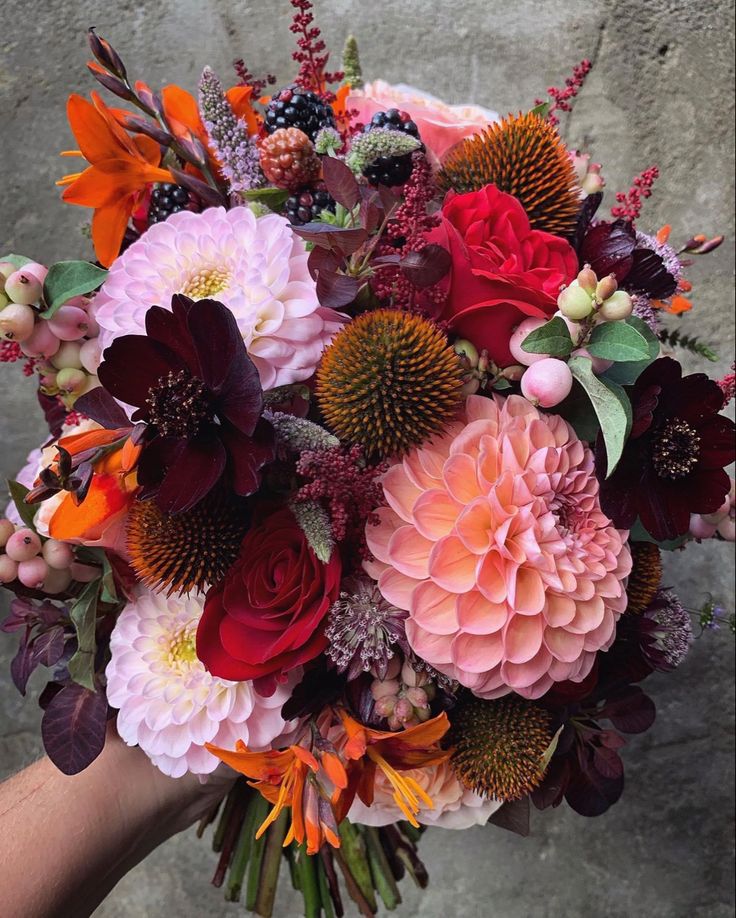 a bouquet of flowers is being held by someone's hand in front of a stone wall