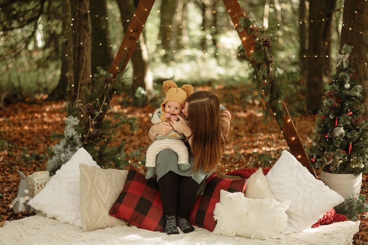 a woman holding a baby in her arms while sitting on a bed covered with pillows