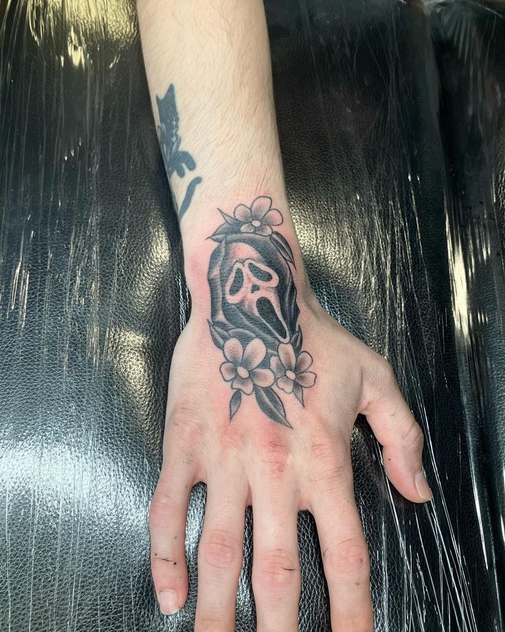 a hand with a skull and flowers tattoo on it