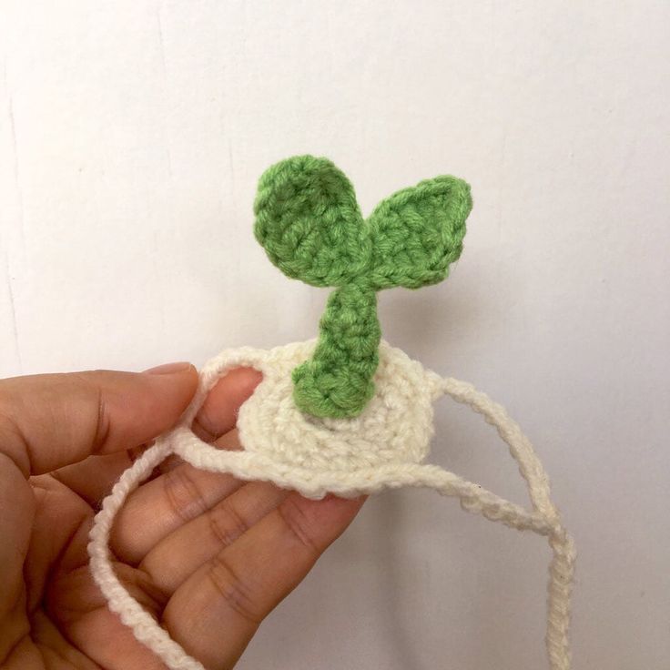 a hand holding a small crocheted plant on top of a white string with green leaves