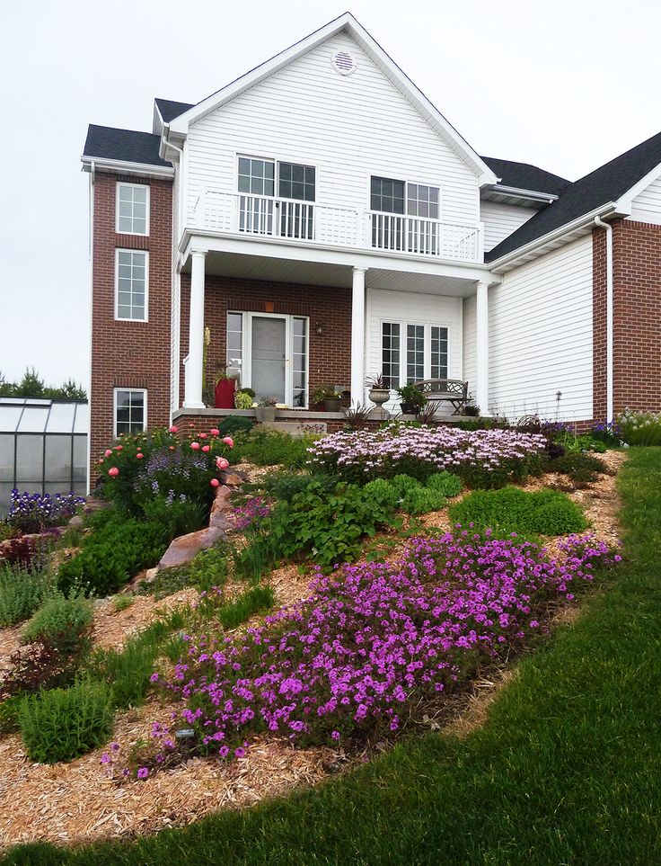 a white house with purple flowers in the foreground and green grass on the ground