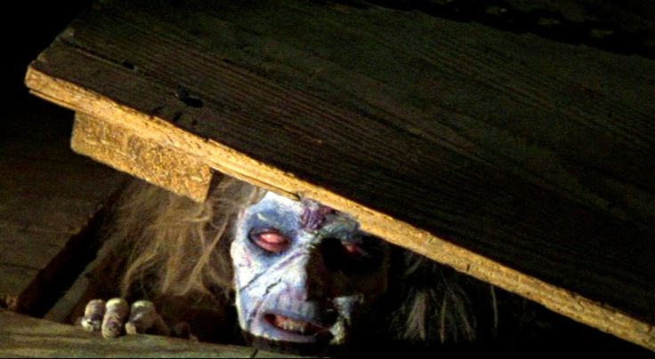 a creepy clown with makeup on peeking out from under a wooden structure in the dark