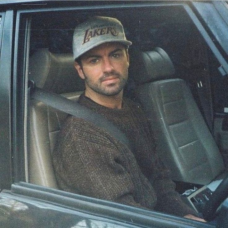 a man sitting in the driver's seat of a car wearing a lakers hat