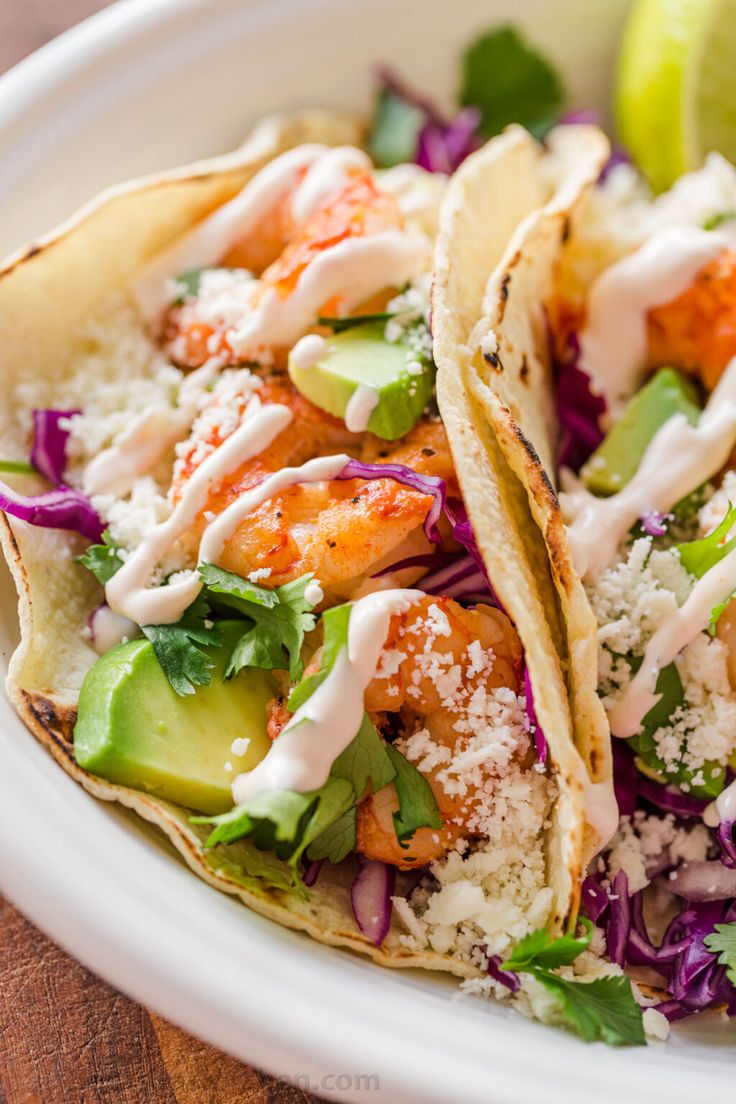 two shrimp tacos with cole slaw and lime wedges in a white bowl