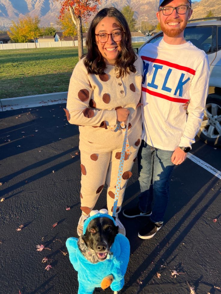 a man and woman standing next to a dog on a leash in the parking lot