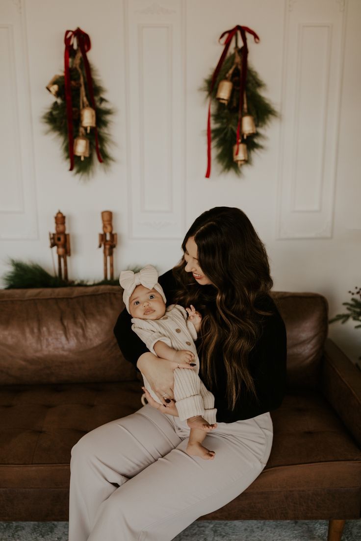 a woman holding a baby in her arms while sitting on a couch with christmas decorations