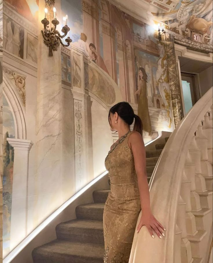 a woman in a gold dress is standing on the stairs with her hand on her hip