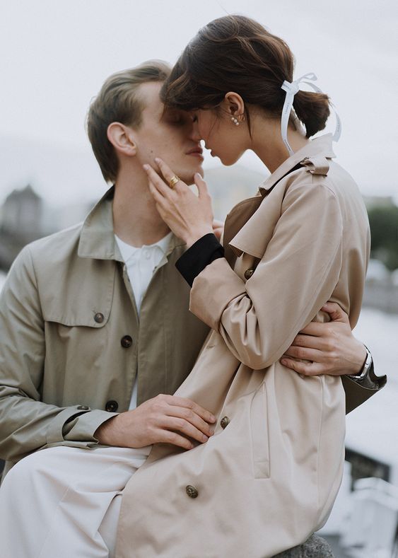 a man and woman kissing each other while sitting on top of a stone bench in front of water