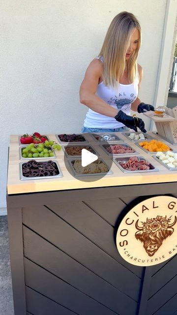 a woman standing behind a counter filled with food