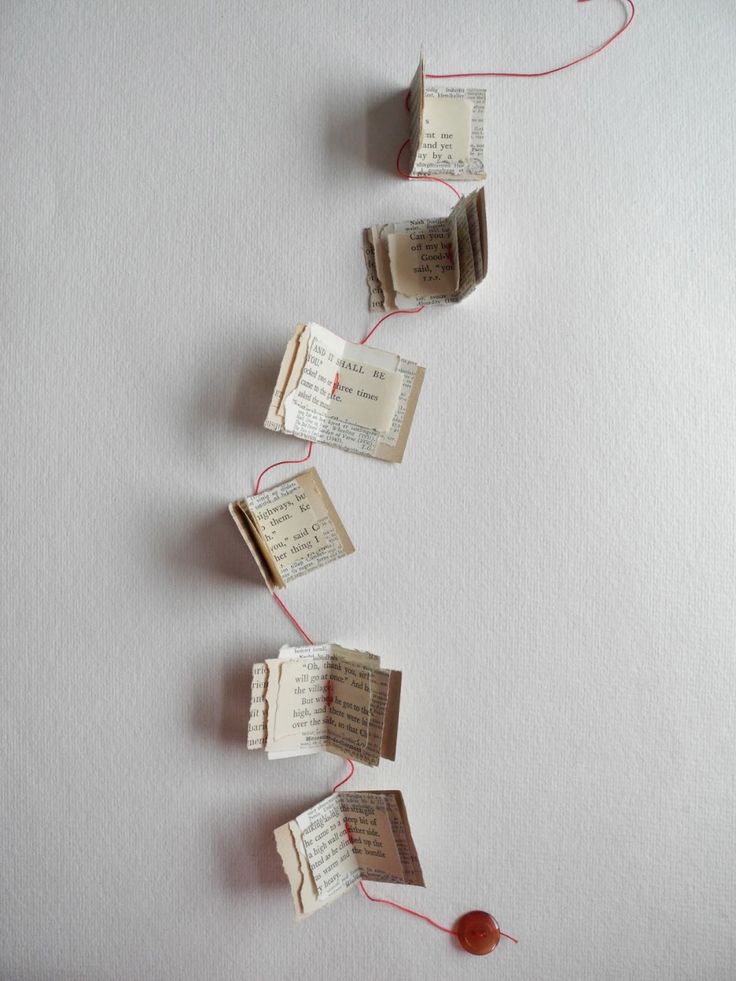 three pieces of paper with string attached to them on a white surface, one has red thread and the other is made out of old book pages