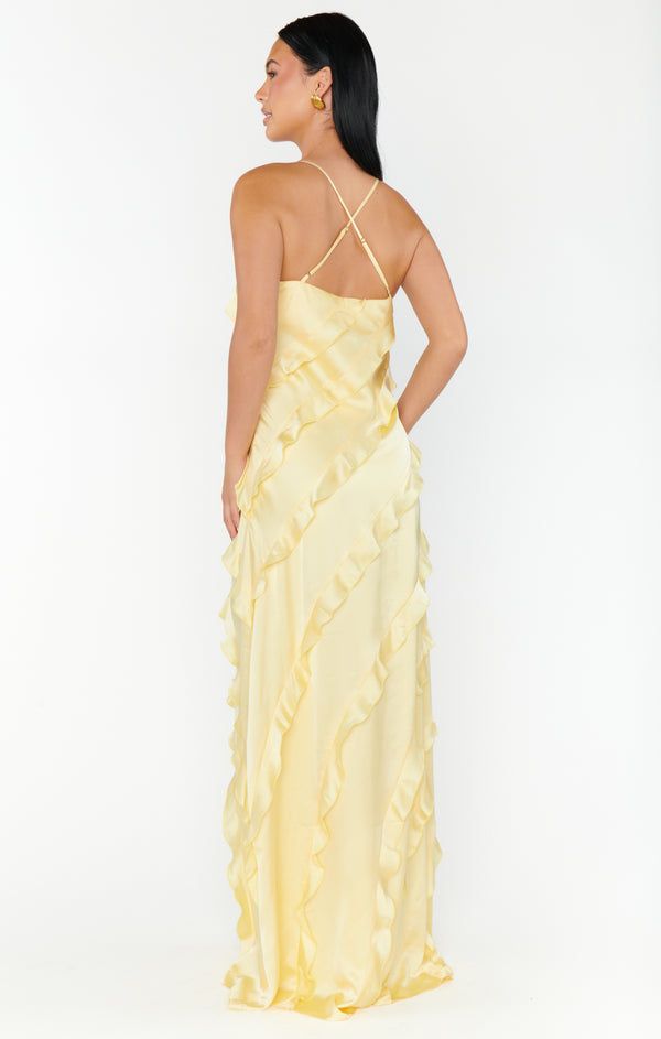 a woman wearing a yellow dress with ruffles on the bottom and back, looking off to the side