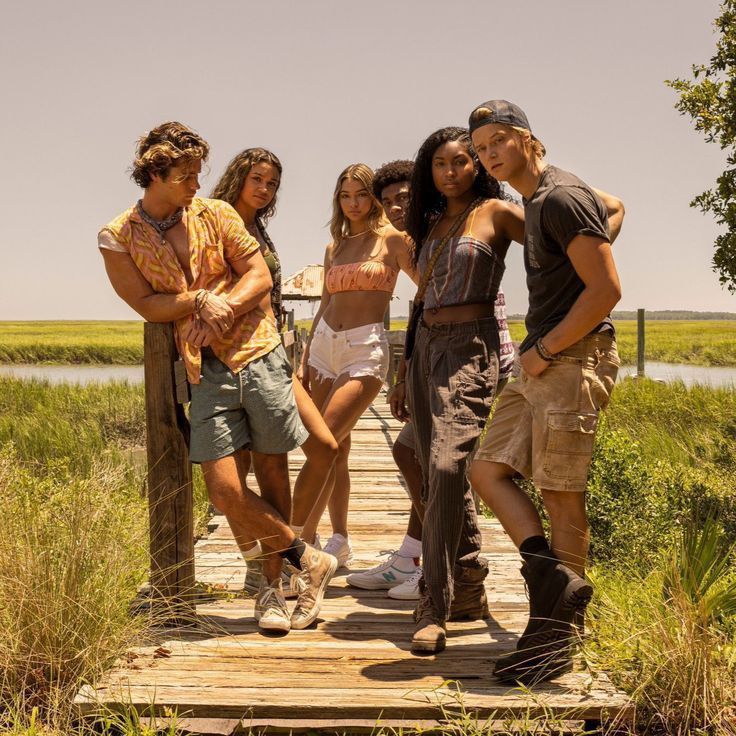 a group of young people standing on a wooden bridge over a marshy area with tall grass