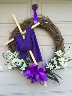 a wreath with purple and white flowers hanging on a garage door next to a pair of crucifixs